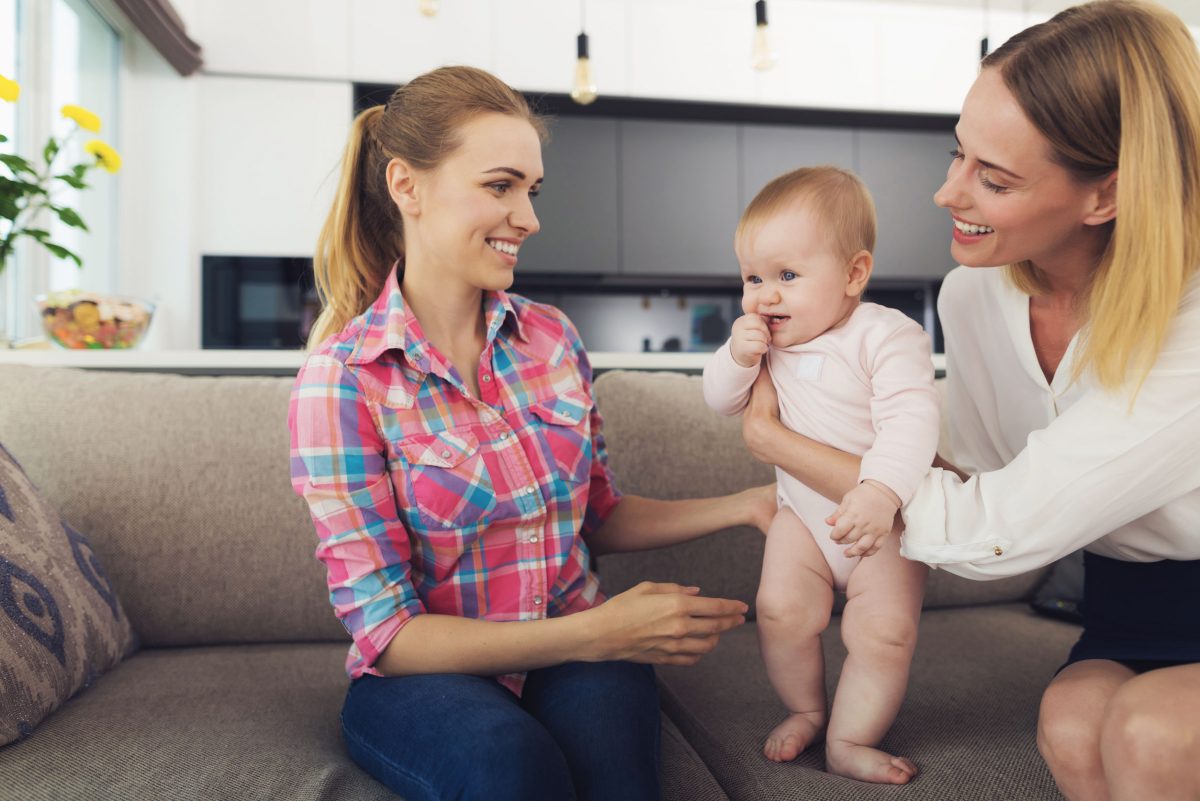 Mother Giving Baby to Nanny Sitting on Sofa.