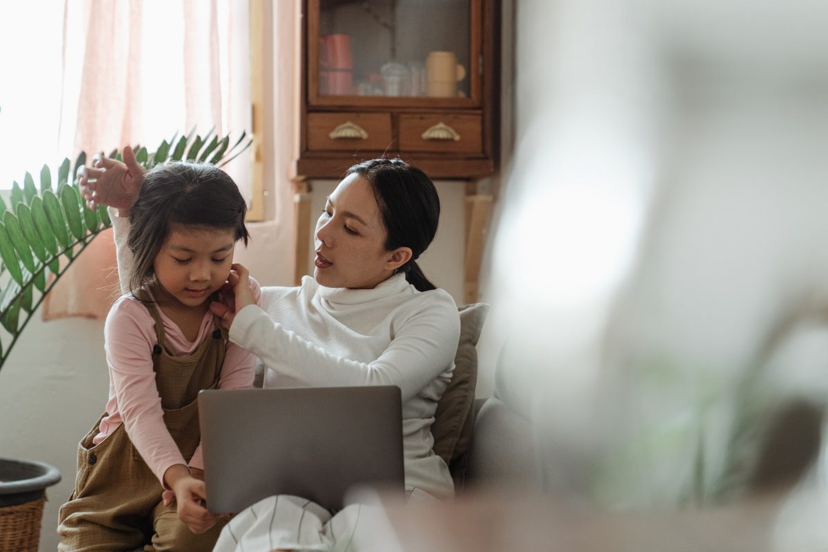 mom researching on computer how to book nannies during winter holidays while she fixes her daughters' hair